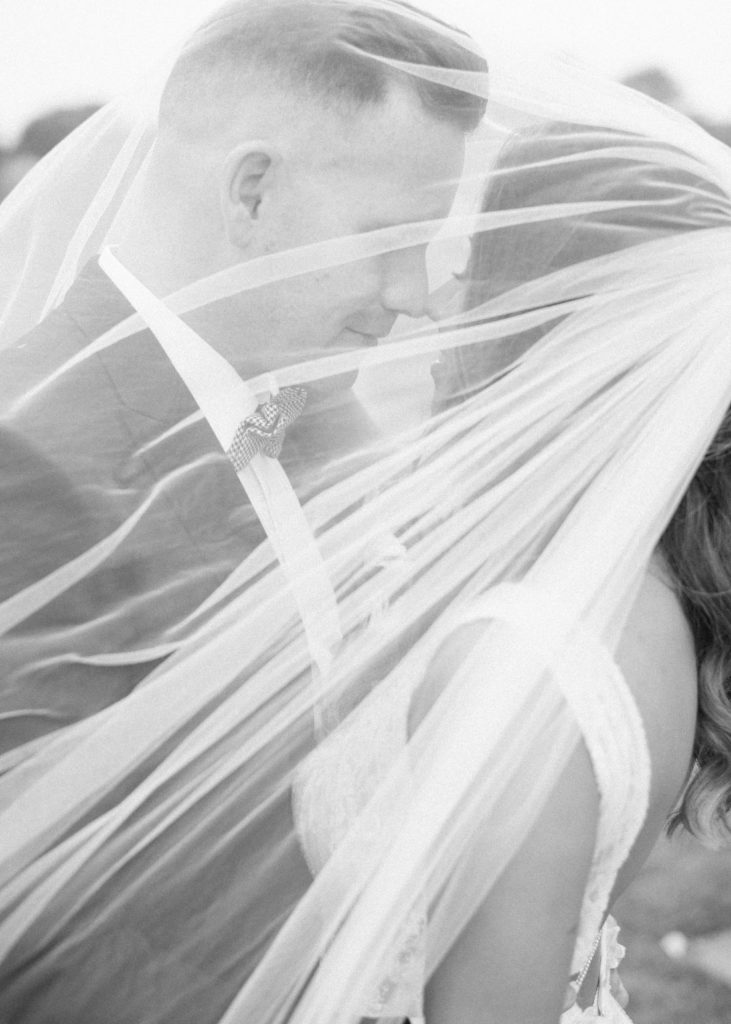 Black and white portrait of newlyweds under the bride's veil in the rain at Killruddery House.