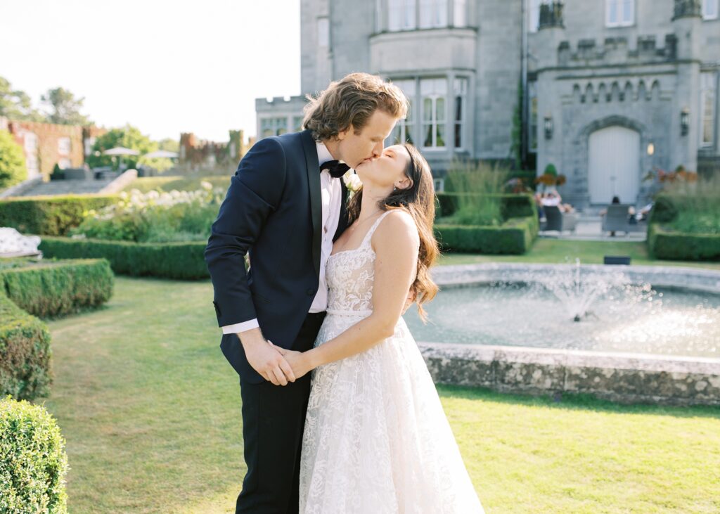 Newlywed couple share a kiss in front of Dromoland Castle Hotel, Ireland.