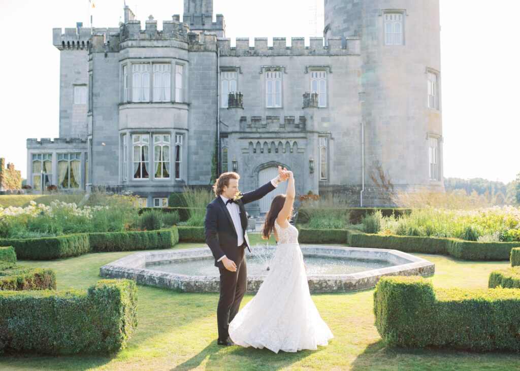 Groom twirls his bride outside Dromoland Castle Hotel during golden hour.