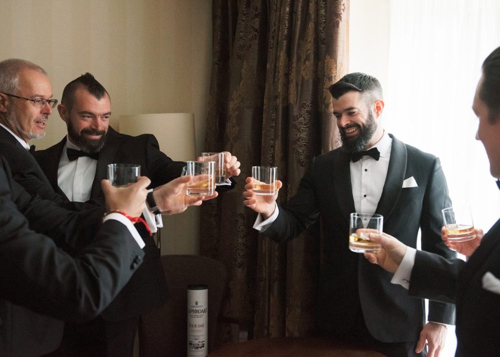 Groom, his brother, father and groomsmen share a toast of whiskey in their room.