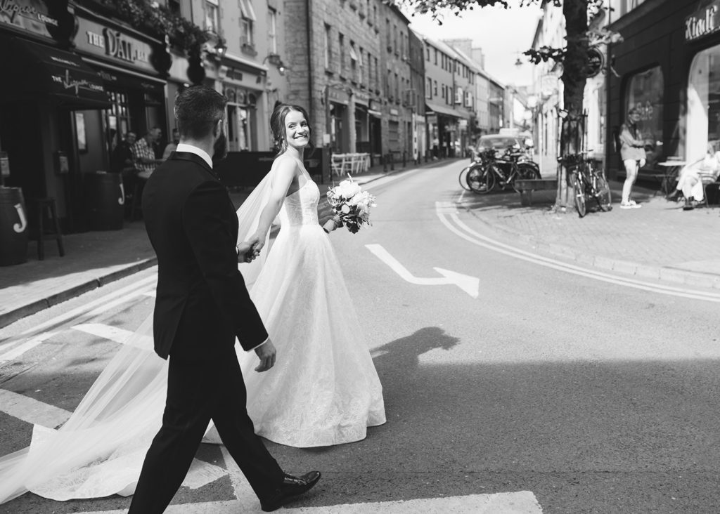 Black and white candid photo of newlywed couple walking in Galway city, Ireland.