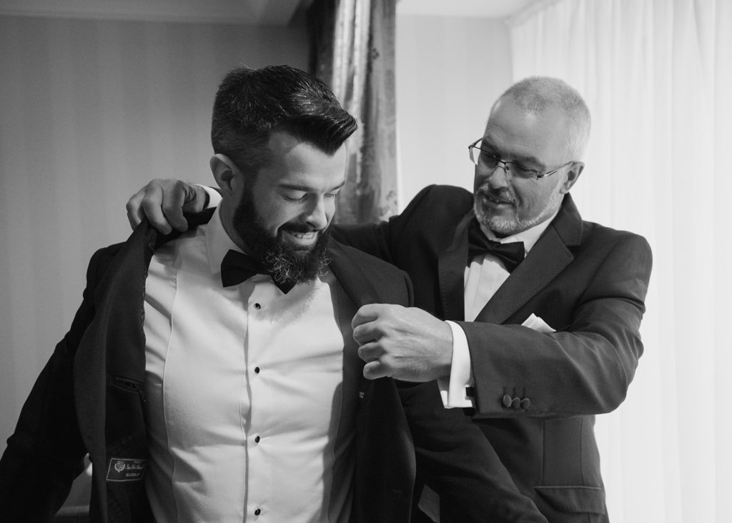 Groom's father helps groom with his jacket in the morning.