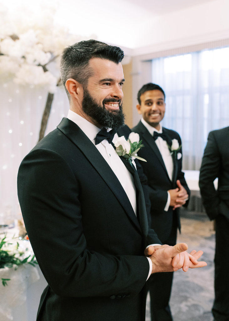 Groom smiling at bride's arrival in wedding ceremony room.