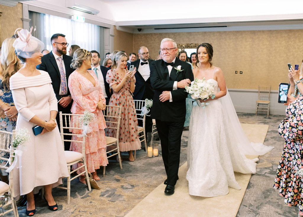 Bride and her father walk down the aisle with adoring guests all around.