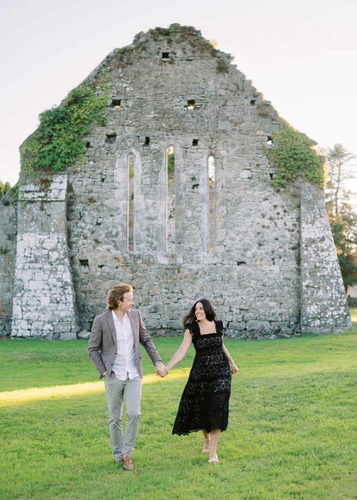 Engaged couple hold hands at sunset in Quin Abbey, Ireland.