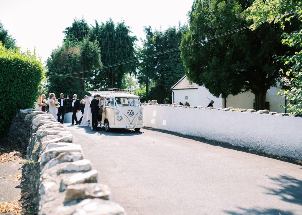 The guests crowd around the newlywed's vintage VW camper van to see them off after their wedding ceremony.