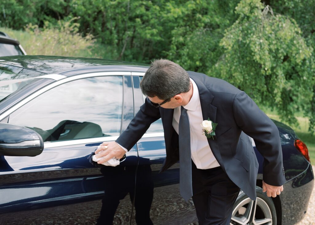 Bride's father proudly polishes his car on the morning of his daughter's summer wedding.
