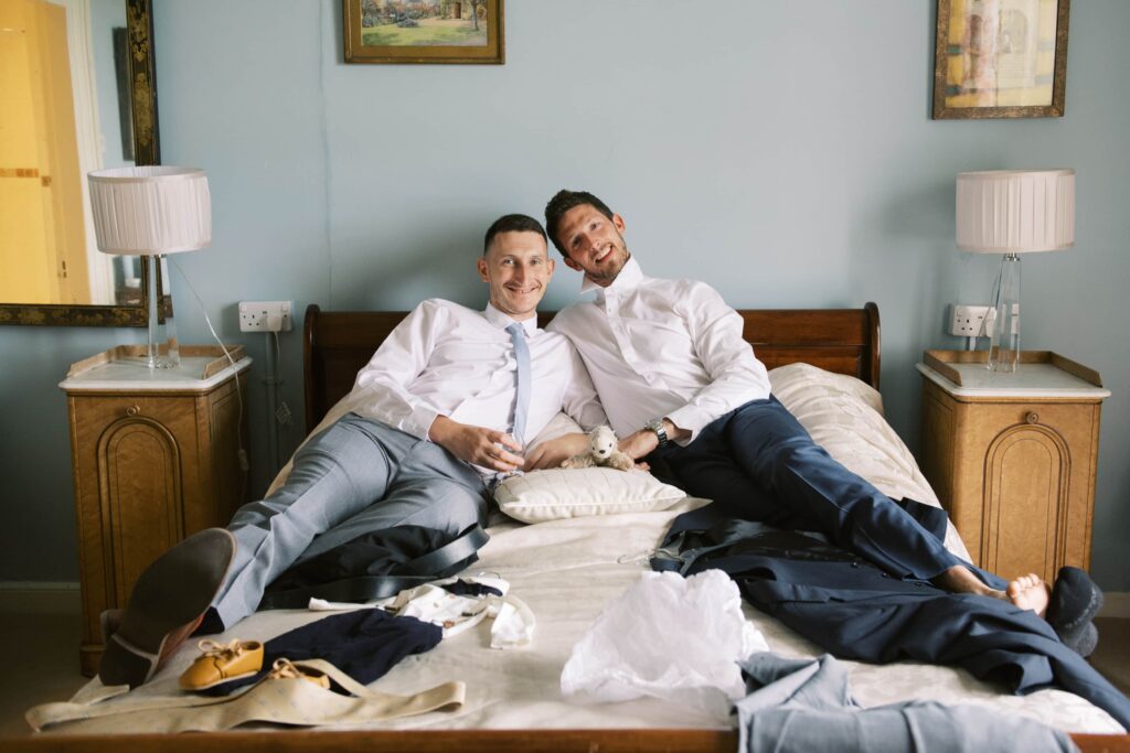 Two groomsmen playfully sitting on the bed together and posing for a funny photo in Temple House.