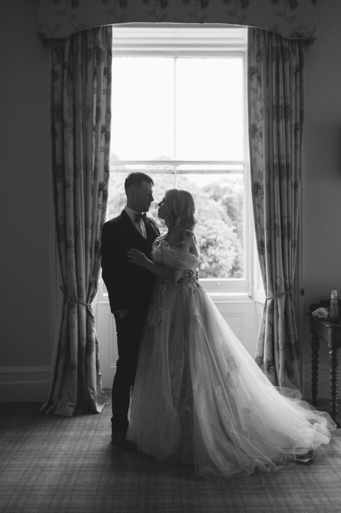 Black and white portrait of the bride and groom sharing a romantic moment in front of a big window in Temple House.