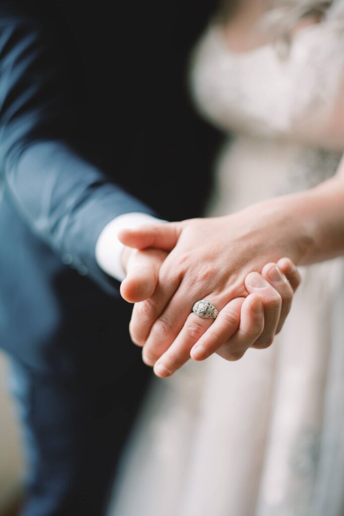 Close-up detail of the eloping Bride and Groom holding hands, with wedding rings in centre stage.