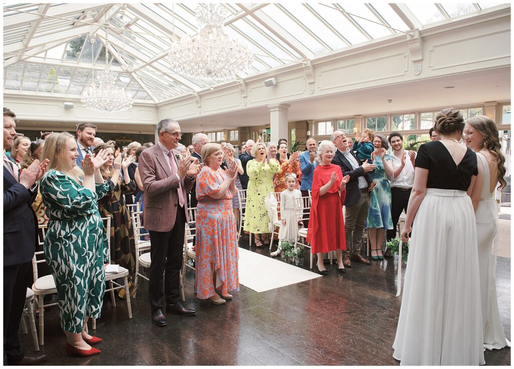 Same-sex wedding photography of ceremony and guests cheering.