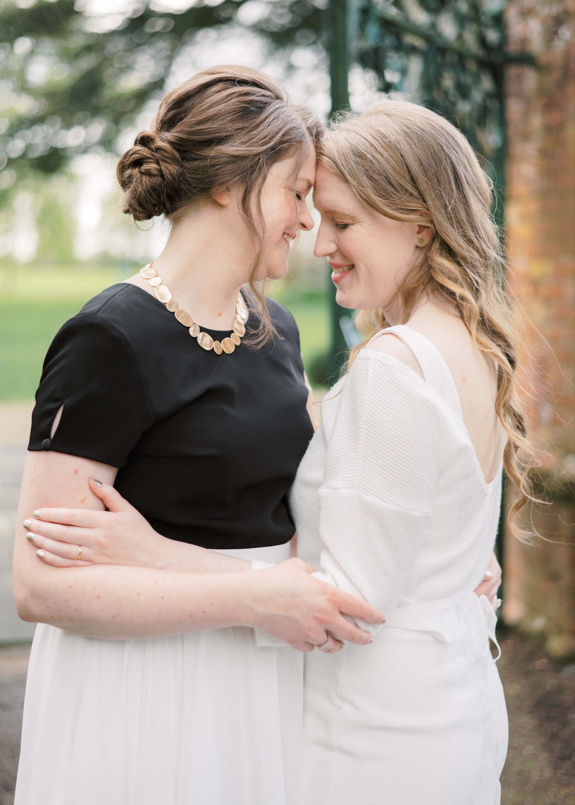 Two brides embrace each other in front of the Walled Garden's main gate.