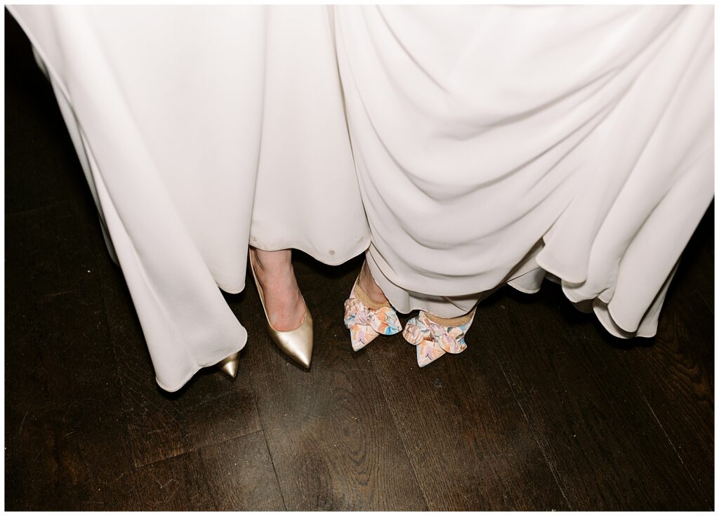 Same-sex couple pose with their heels and wedding dresses at the end of the wedding night.