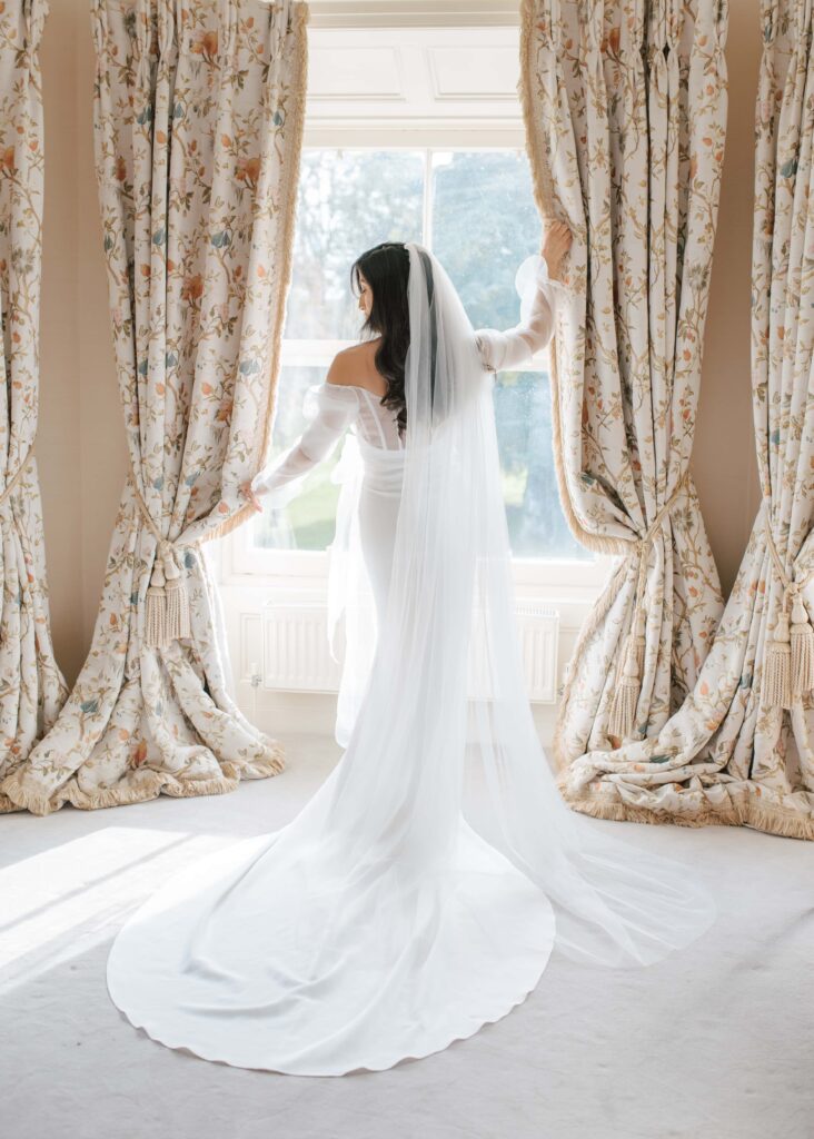 Bride poses in her wedding dress at the bright window.