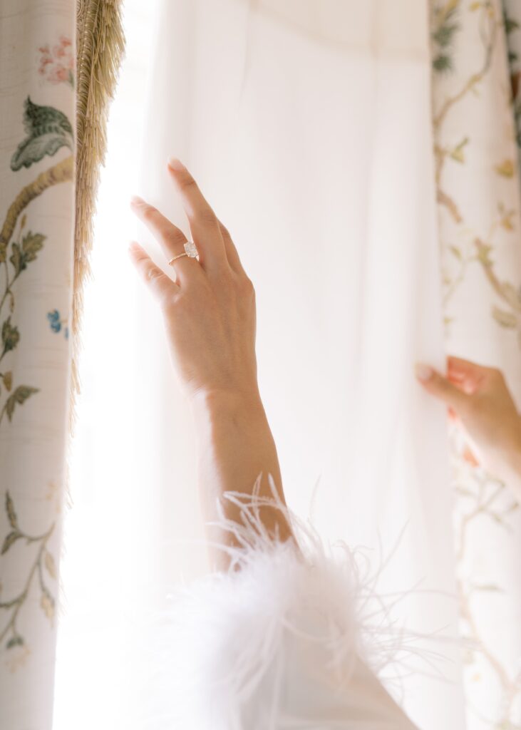 Close up photo of the bride's hands reaching for her beautiful wedding dress hanging in the window.