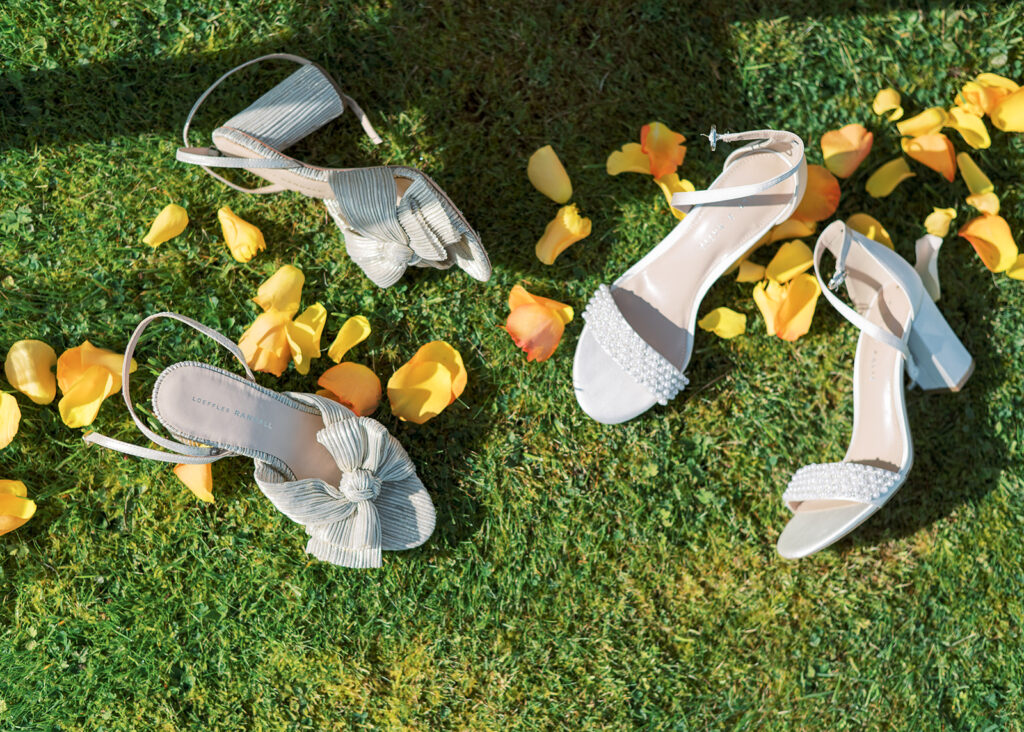 Brides' shoes laid on the grass of the garden wedding ceremony space, with a trail of petals running through.