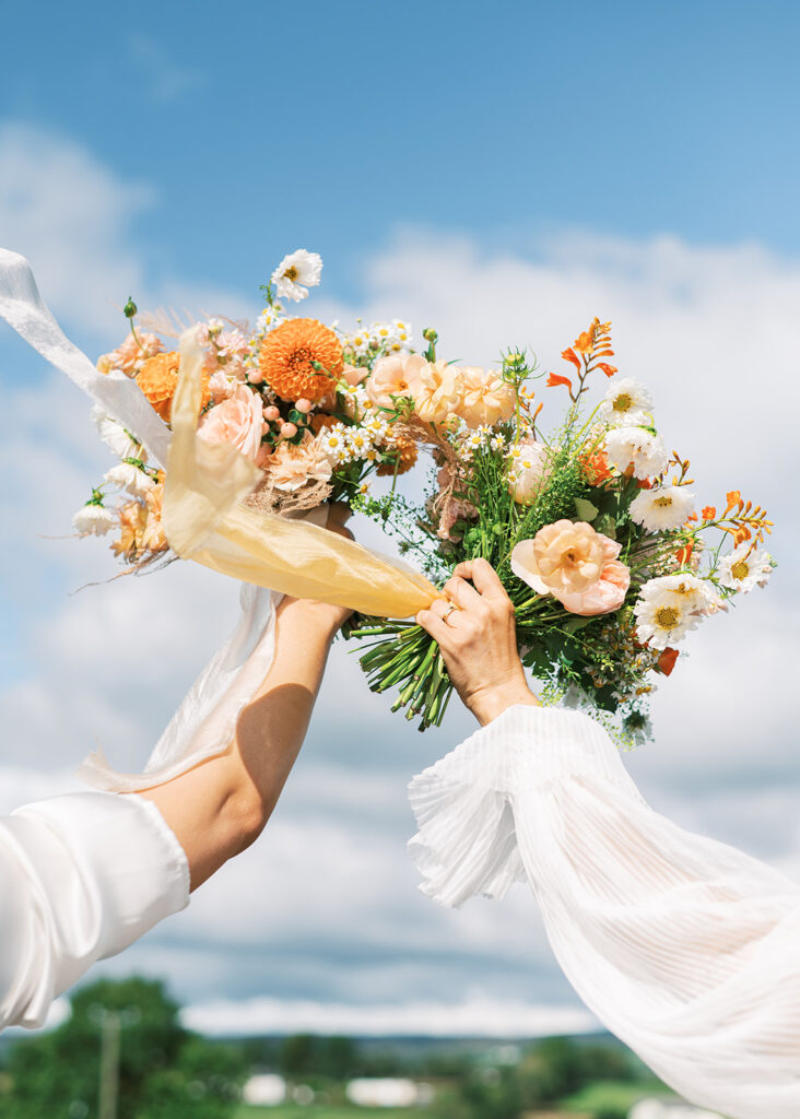 The brides hold their bouquets aloft in the wind.