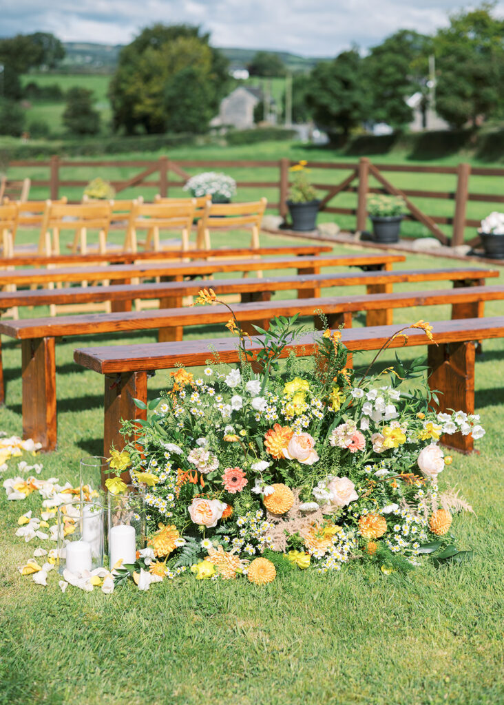 Details of the garden wedding ceremony location, featuring lush bouquets, candles, and trails of flower petals along the aisle.