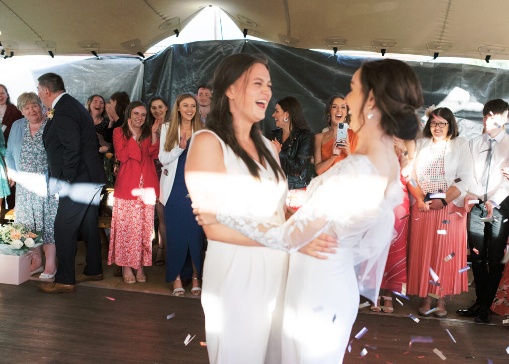 Everyone cheers on the two brides as confetti rains down around their dance.